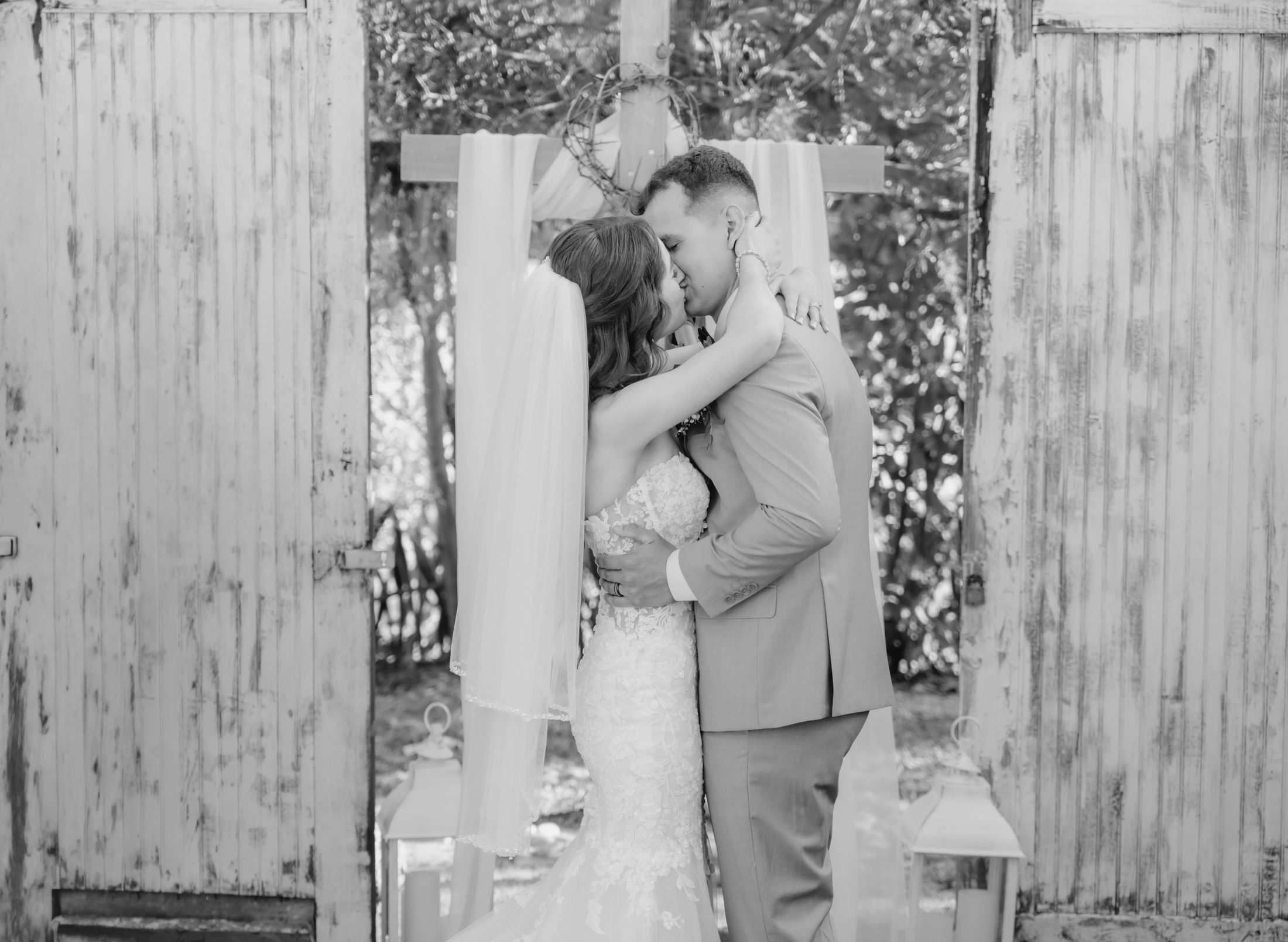 A couple share their first kiss beneath a cross in warm black and white