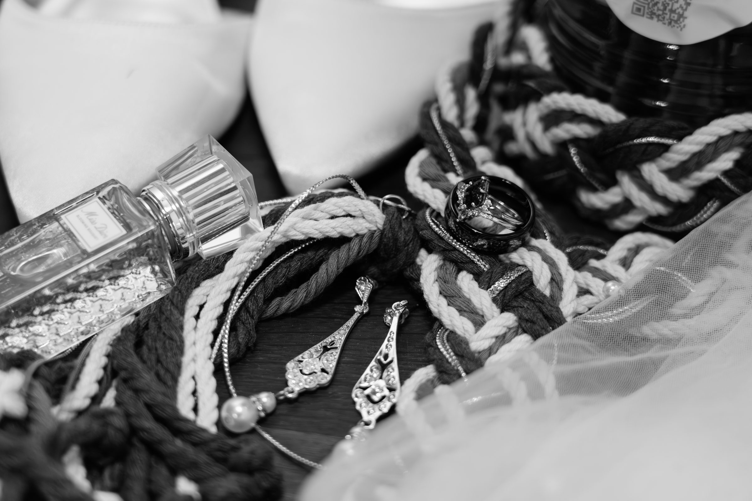 Bridal details in black and white: the emerald wedding rings resting on a braided handfasting cord, with the bride's shoes, earrings, and Miss Dior perfume, documentary wedding photography by GM Productions