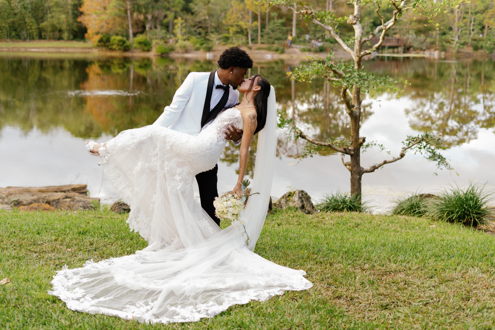 Bride and groom by the lake, veil and train sweeping across the grass