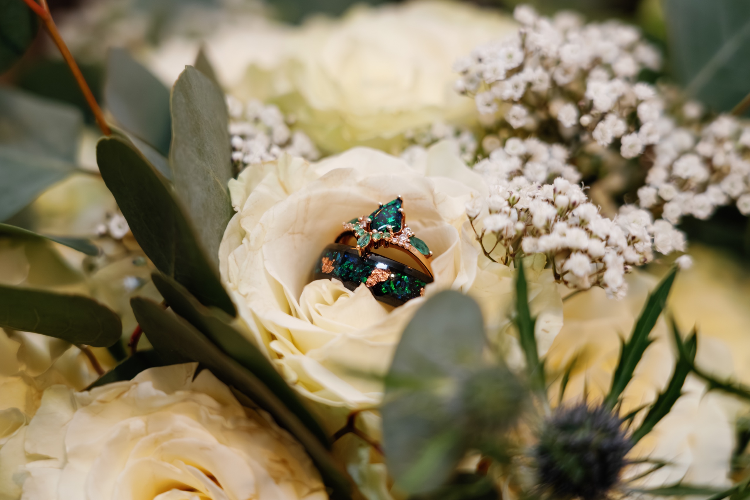 Emerald opal wedding bands nestled in ivory roses and baby's breath, photographed by GM Productions at Kelly and Taylor's wedding